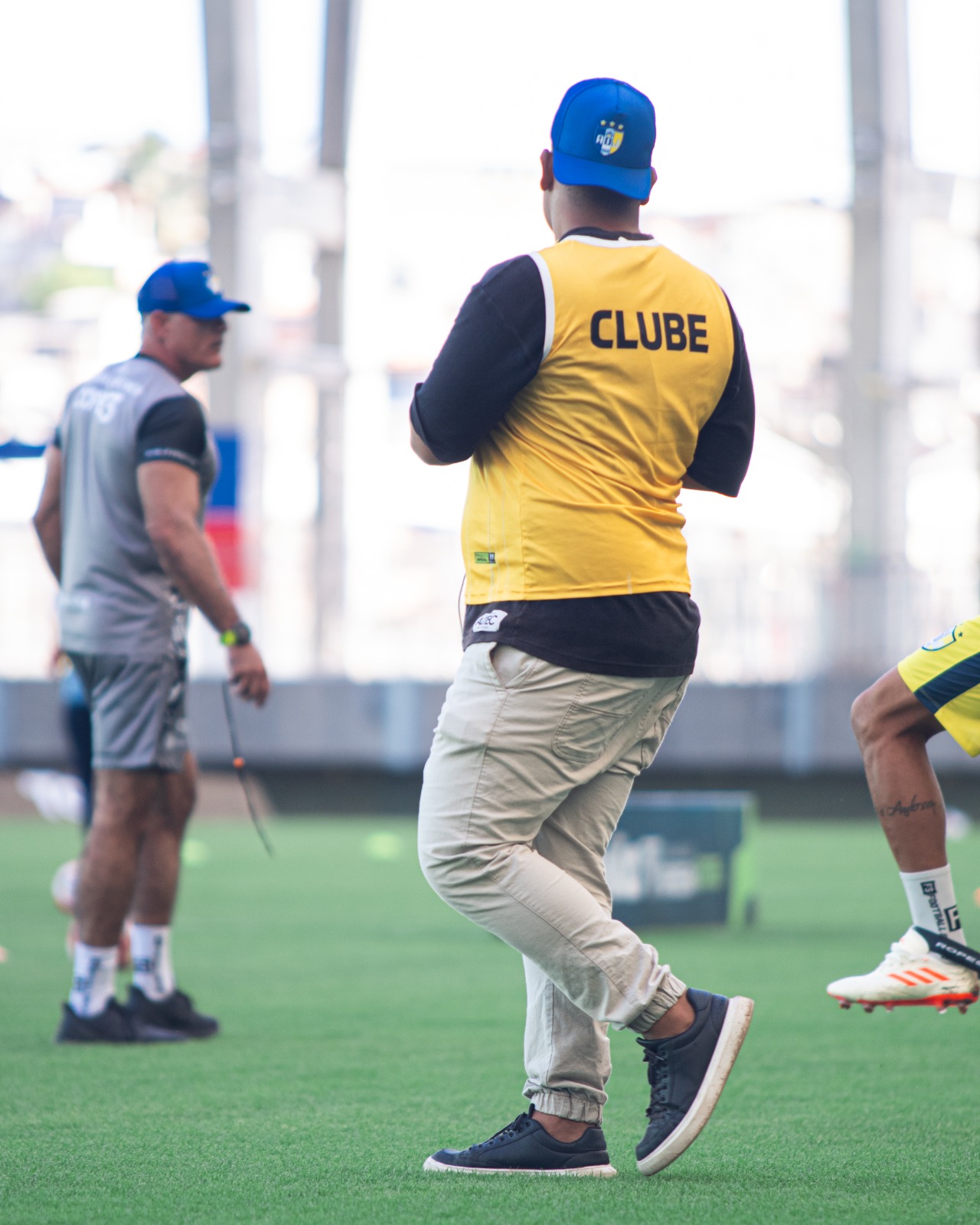 Samuel Moraes de costas com colete amarelo escrito Clube durante treino em campo